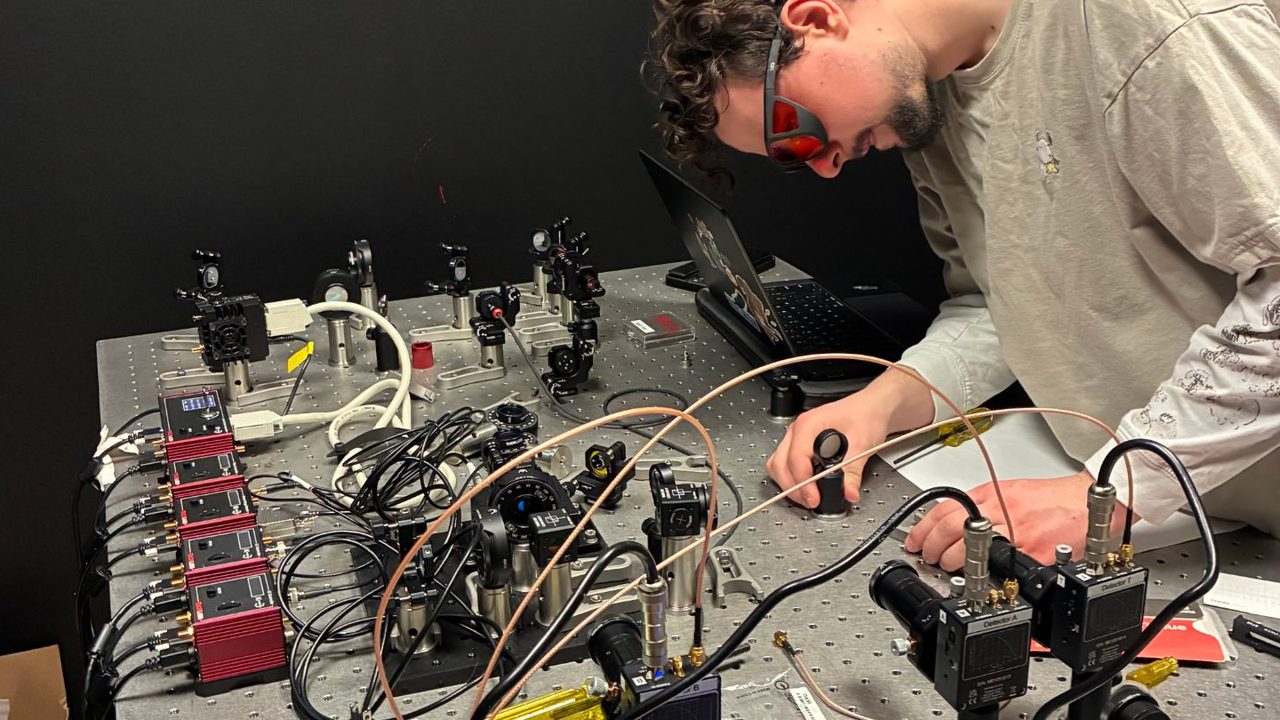 Zach in laser safety glasses leaning over an optics table, adjusting a mount